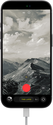iPhone 18 Pro, pohled zepředu, na displeji je hornatá krajina, režim časosběrného videa s otevřeným výběrem režimů fotoaparátu, k nabíjecímu portu je připojený napájecí kabel