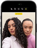 iPhone 18 Pro, černý, pohled zepředu, na displeji jsou dvě pózující osoby jako ukázka Center Stage přední kamery