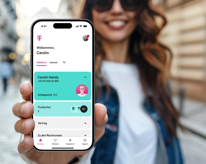 Eine Frau steht in einer Stra��e und zeigt die Vertrags��bersicht der MeinMagenta App auf ihrem Smartphone.