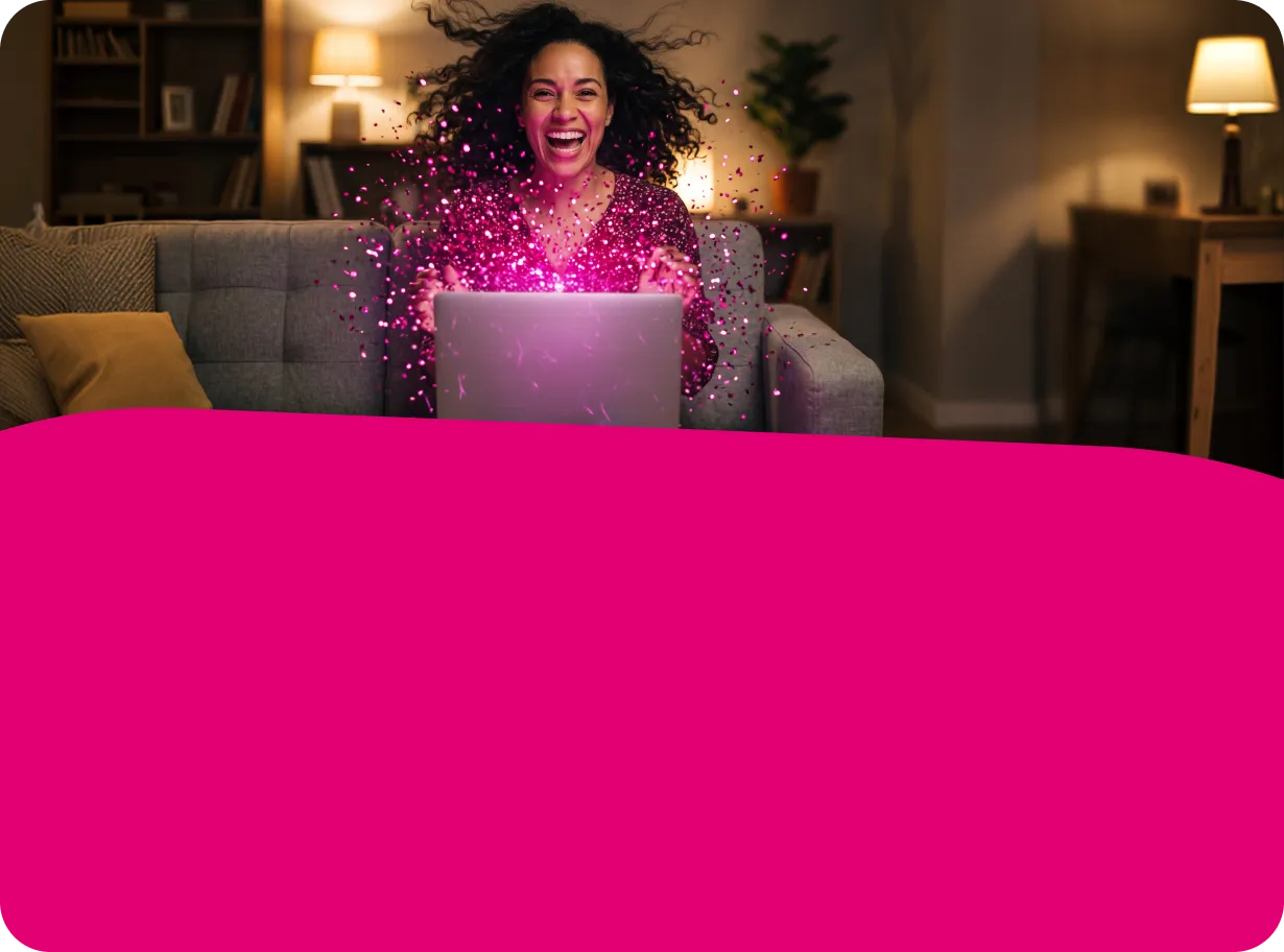 Eine lachende Frau sitzt auf einem Sofa, vor ihr ein aufgeklappter Laptop, aus dem pinkfarbener Glitzer sprüht.