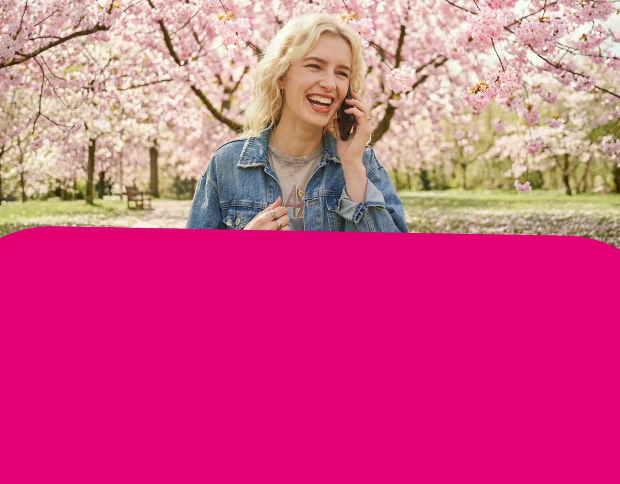 Lachende Frau telefoniert vor blühenden Bäumen.