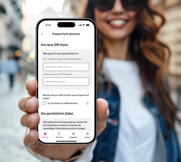 A woman stands on a street and shows the setup page of the MeinMagenta app on her smartphone.