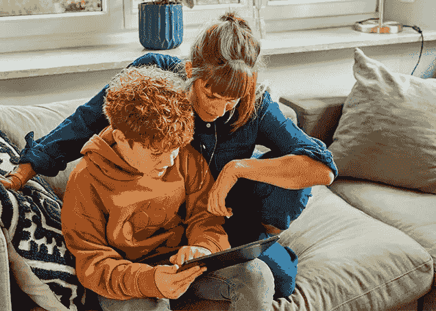 Frau und Sohn sitzen auf einem Sofa und blicken auf ein Tablet